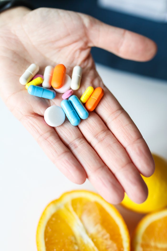 about-01 Hand holding colorful pills next to fresh orange slices, promoting health and vitamin intake.
