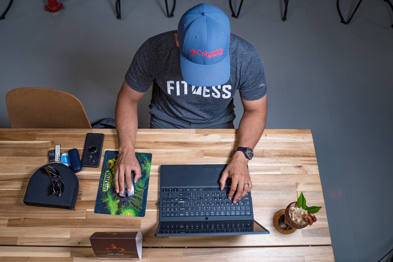 gallery-5 Overhead view of a man with a cap working on a laptop in a cafe with a drink on the table.