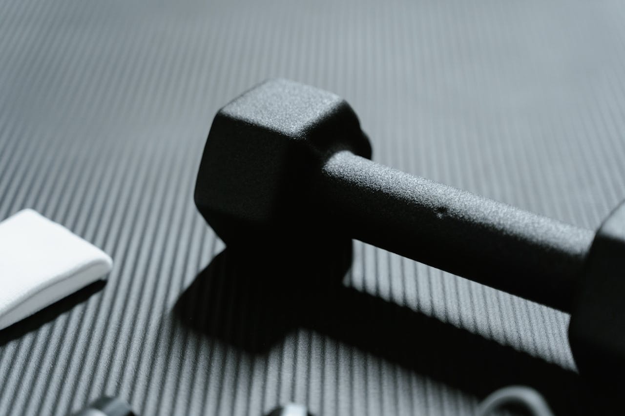 gallery-4 Detailed view of a black dumbbell on textured mat for fitness workout