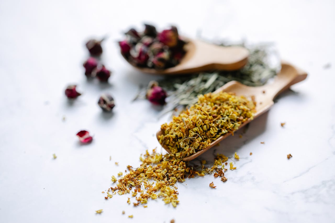 gallery-1 Close-up of dried herbs and flowers in wooden spoons on a marble surface.